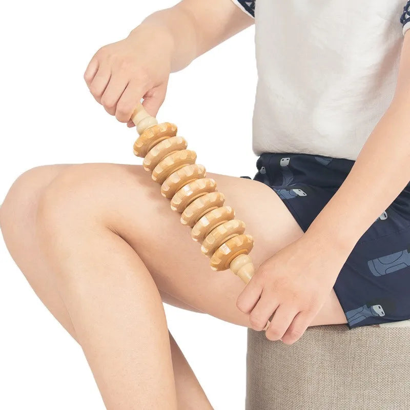 Person using a wooden massage stick on their leg against a white background
